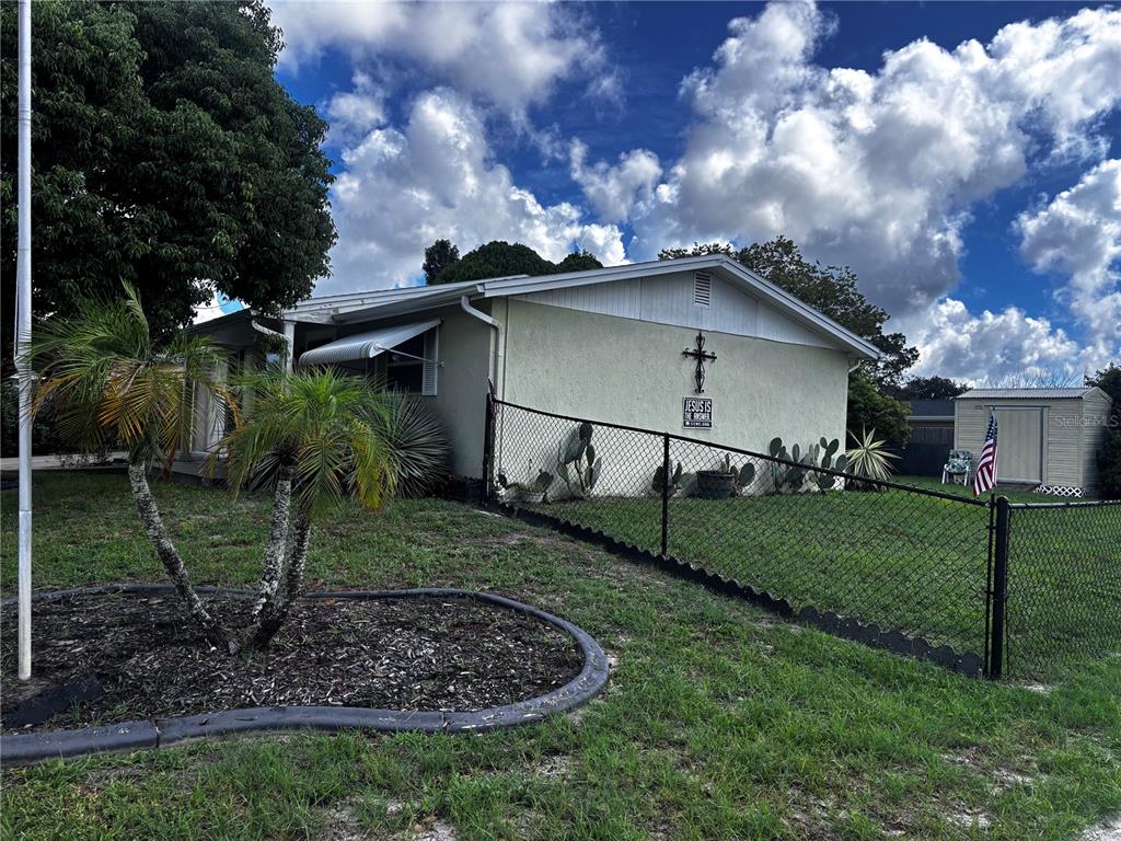 A single-story house with a chain-link fence, a cross wall decoration, and a shed — 9040 CHATAM LANE, PORT RICHEY, FL