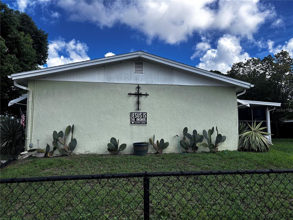 A light green house exterior features a metal cross and a sign on the wall — 9040 CHATAM LANE, PORT RICHEY, FL