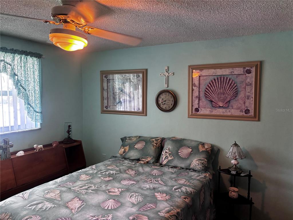 A bedroom features a seashell-patterned bedspread, light blue walls, and a ceiling fan — 9040 CHATAM LANE, PORT RICHEY, FL