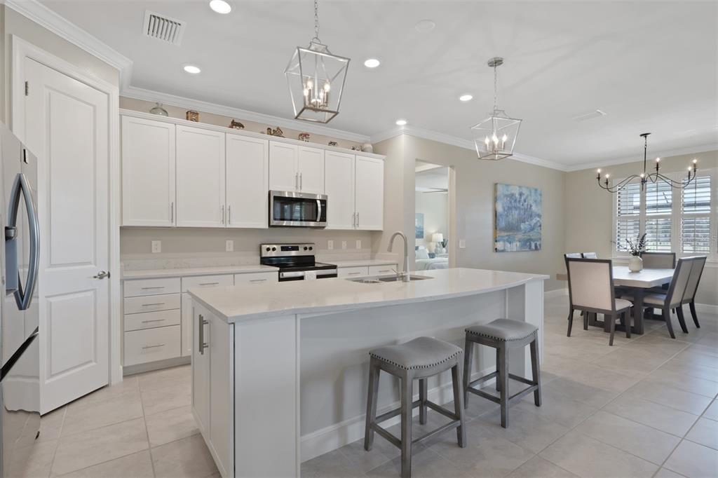 A modern kitchen features white cabinets, a quartz island with bar stools, and pendant lighting — 3425 HAMPTON BOULEVARD, ALVA, FL