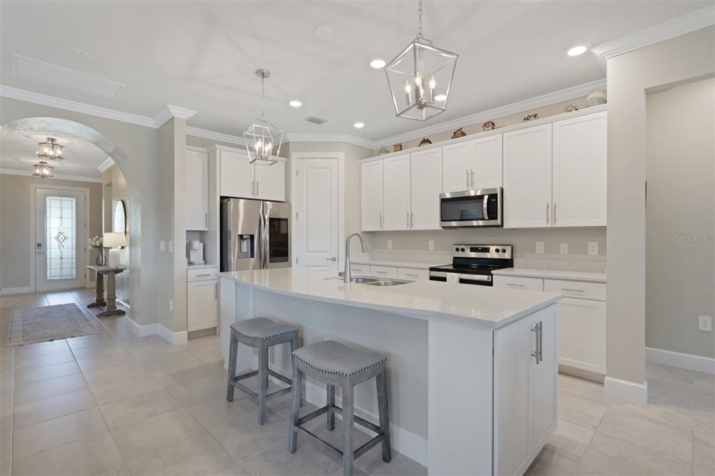A kitchen with white cabinets, a quartz island, stainless steel appliances, and gray bar stools — 3425 HAMPTON BOULEVARD, ALVA, FL