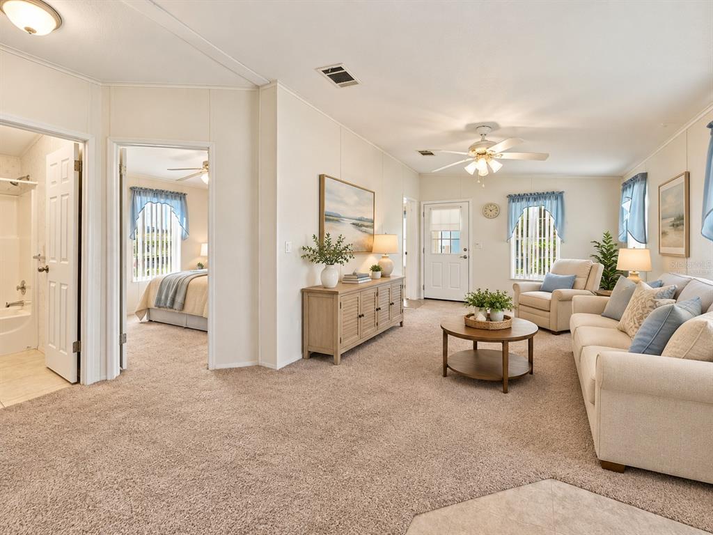 A living room with beige carpet, a sofa, armchair, coffee table, and an adjacent bedroom — 59 BEAVERKILL DRIVE, LAKE WALES, FL