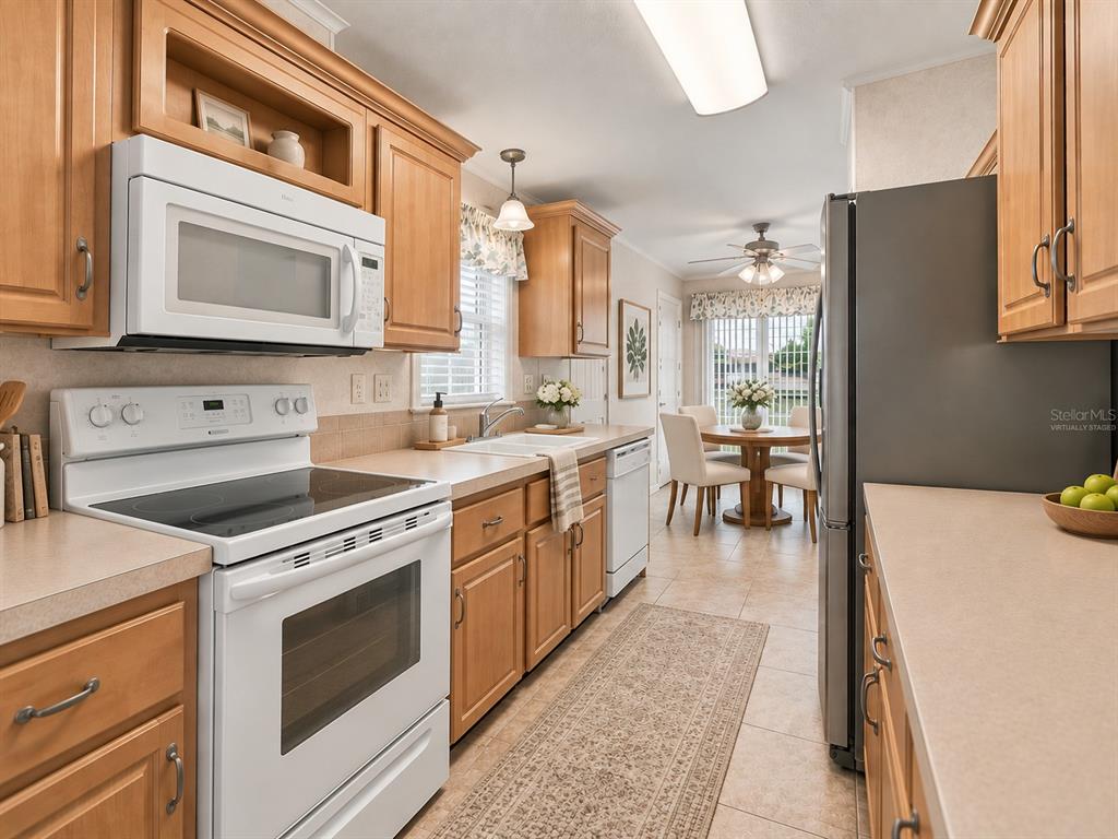 A kitchen with light wood cabinets, white appliances, and a dining area in the background — 59 BEAVERKILL DRIVE, LAKE WALES, FL