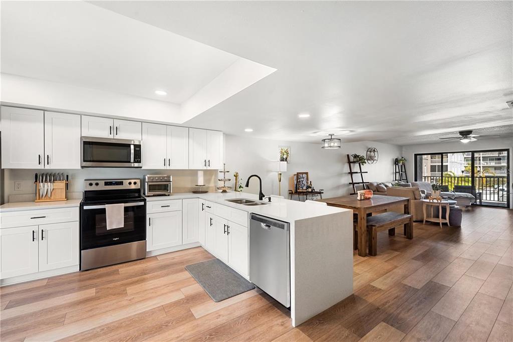 A kitchen features white cabinets, stainless steel appliances, and light wood-look flooring — 745 PINELLAS BAYWAY S UNIT 106, TIERRA VERDE, FL