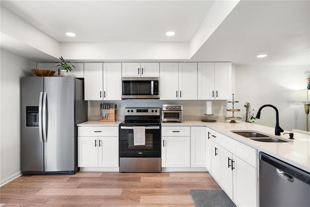 A modern kitchen with white cabinets and stainless steel appliances overlooks a living area — 745 PINELLAS BAYWAY S UNIT 106, TIERRA VERDE, FL