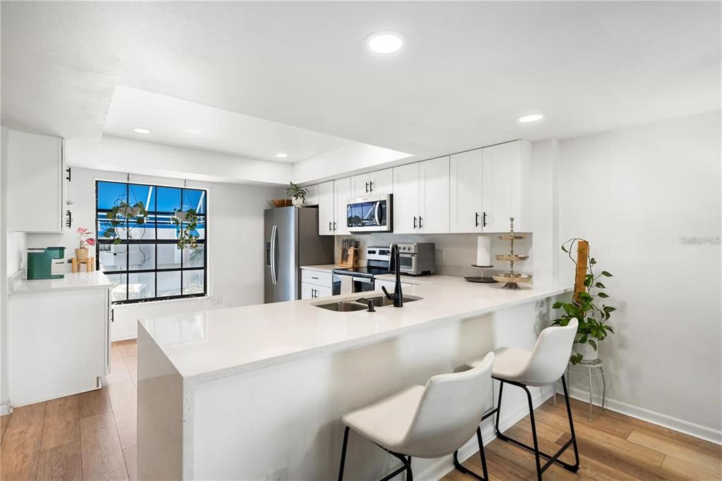 A white kitchen island with a double sink overlooks an open-concept living and dining area — 745 PINELLAS BAYWAY S UNIT 106, TIERRA VERDE, FL