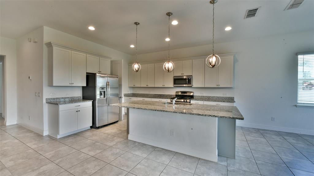 A kitchen features light-colored cabinetry, granite countertops, stainless steel appliances, and a central island — 9152 OLMO COURT, DAVENPORT, FL