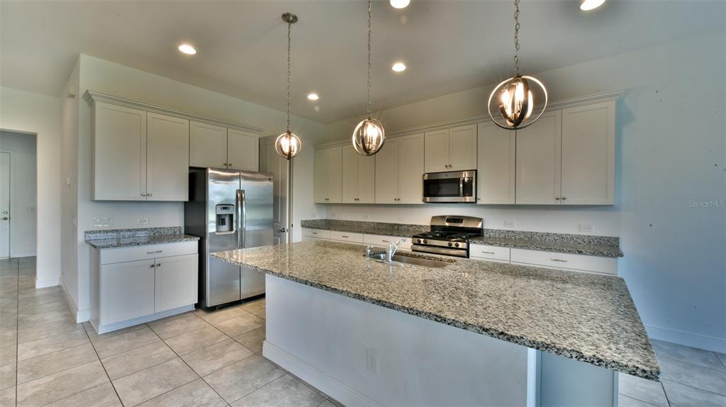 A kitchen features light-colored cabinetry, granite countertops, stainless steel appliances, and a large central island — 9152 OLMO COURT, DAVENPORT, FL
