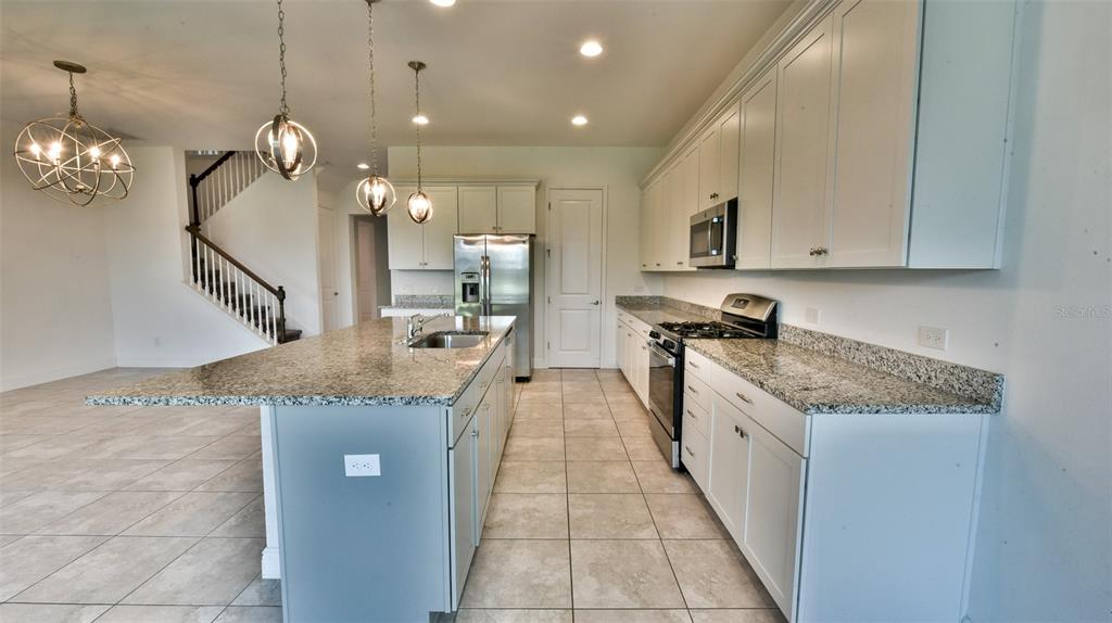 A kitchen features white cabinets, granite countertops, a center island, and a staircase nearby — 9152 OLMO COURT, DAVENPORT, FL