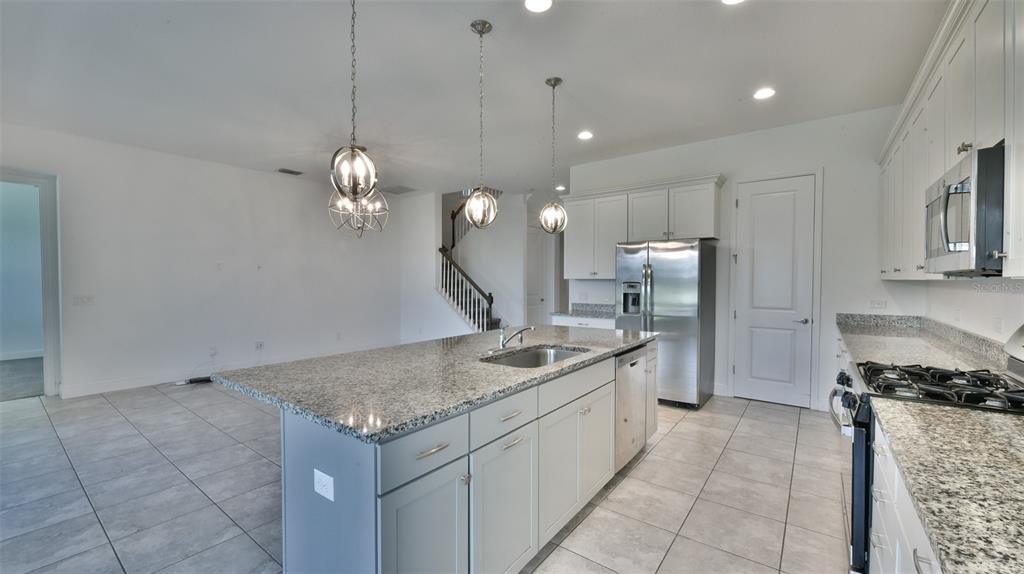A kitchen features a granite-topped island, stainless steel appliances, white cabinetry, and tile flooring — 9152 OLMO COURT, DAVENPORT, FL