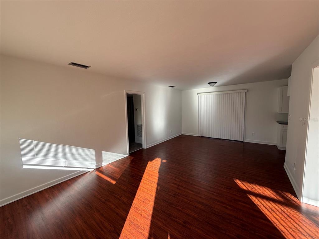 An empty living room features dark wood-look flooring, white walls, and sliding glass patio doors — 536 NE 12TH COURT, GAINESVILLE, FL