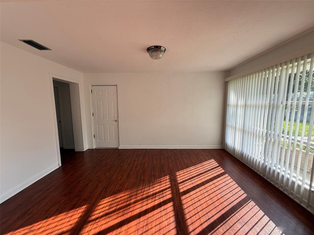 An empty room with wood-look flooring, white walls, a ceiling light, and vertical window blinds — 536 NE 12TH COURT, GAINESVILLE, FL