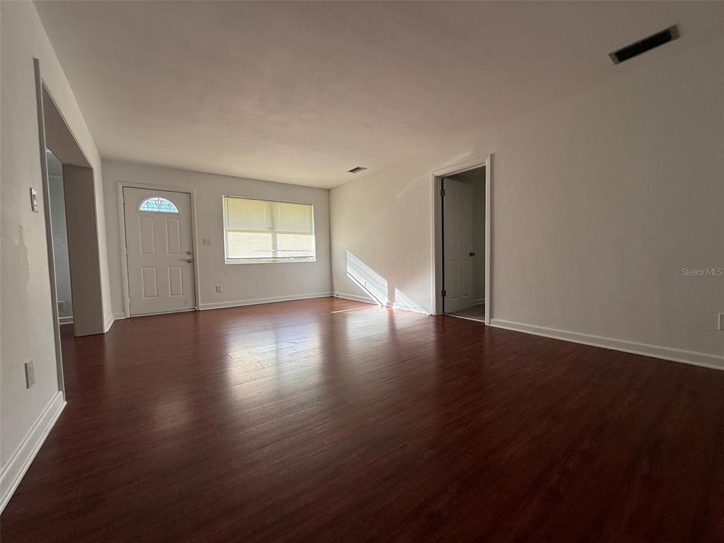 An empty room features dark wood-look flooring, white walls, a front door, and a window — 536 NE 12TH COURT, GAINESVILLE, FL