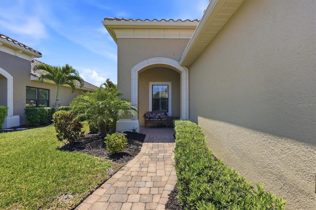 A paved walkway leads to a covered entryway with a bench beside a house exterior — 1359 BACKSPIN DRIVE, ENGLEWOOD, FL