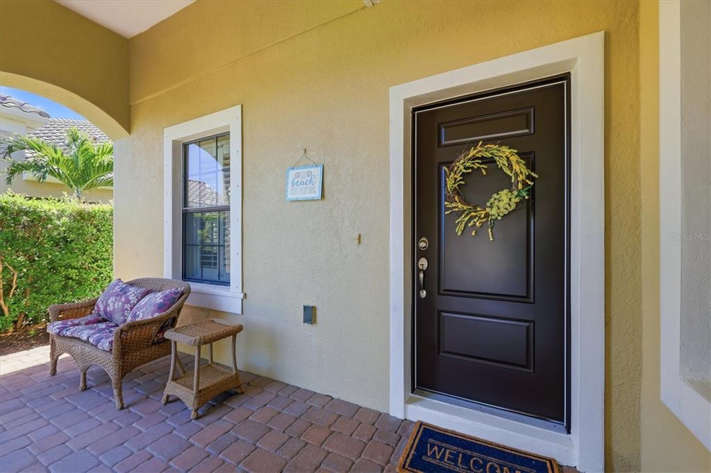 A covered porch features a dark front door, a wicker chair, and a small side table — 1359 BACKSPIN DRIVE, ENGLEWOOD, FL