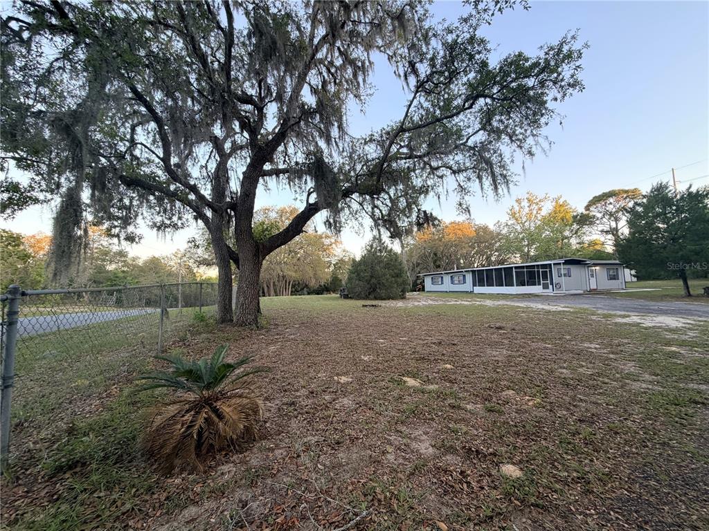 A gravel driveway leads to a paved road bordered by trees and chain-link fencing — 4880 N HIGHLAND PARK DRIVE, HERNANDO, FL
