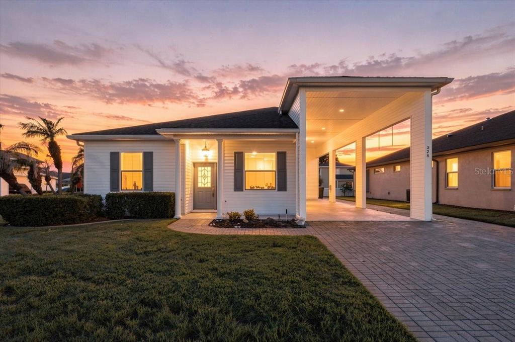 A white single-story house with a paved driveway and an attached carport at sunset — 328 MOTORCOACH DRIVE S, POLK CITY, FL