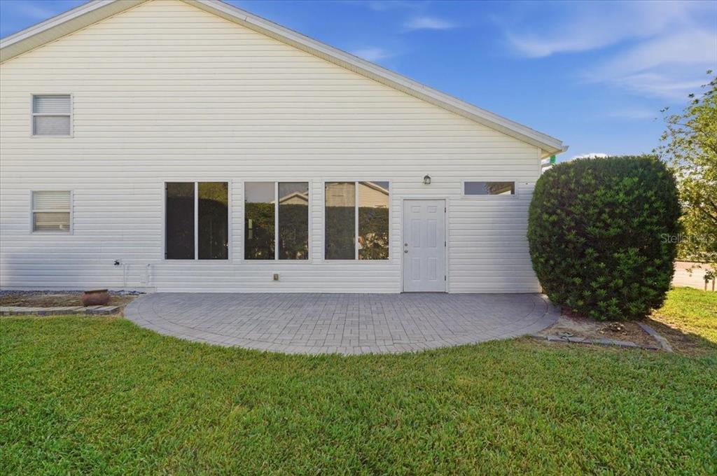 The exterior of a house features white siding, a paved patio, and a large green bush — 328 MOTORCOACH DRIVE S, POLK CITY, FL
