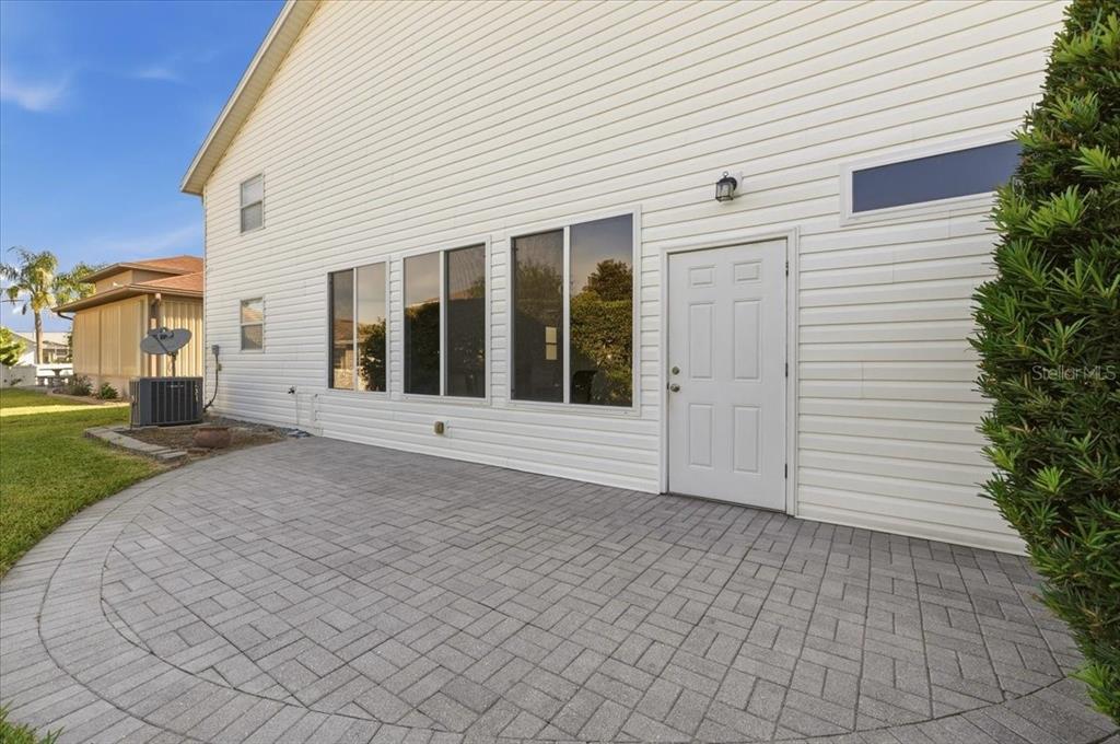 A paved patio sits beside the white vinyl-sided exterior of a house with several windows — 328 MOTORCOACH DRIVE S, POLK CITY, FL