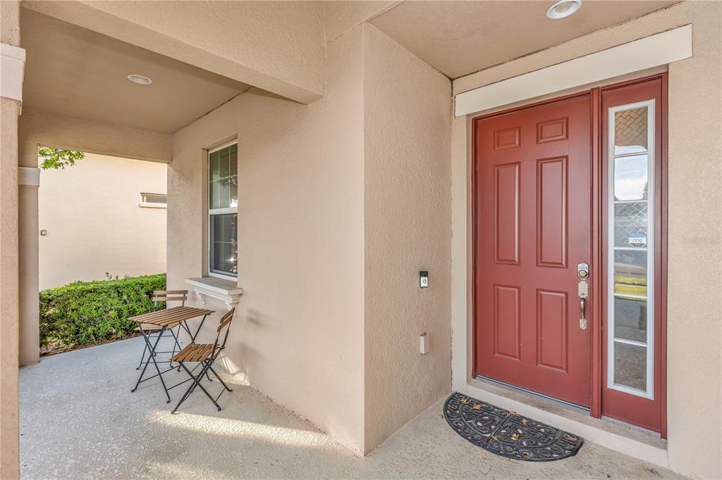 A covered porch features a red front door, a small bistro set, and a window — 3301 BETHPAGE LOOP, MOUNT DORA, FL
