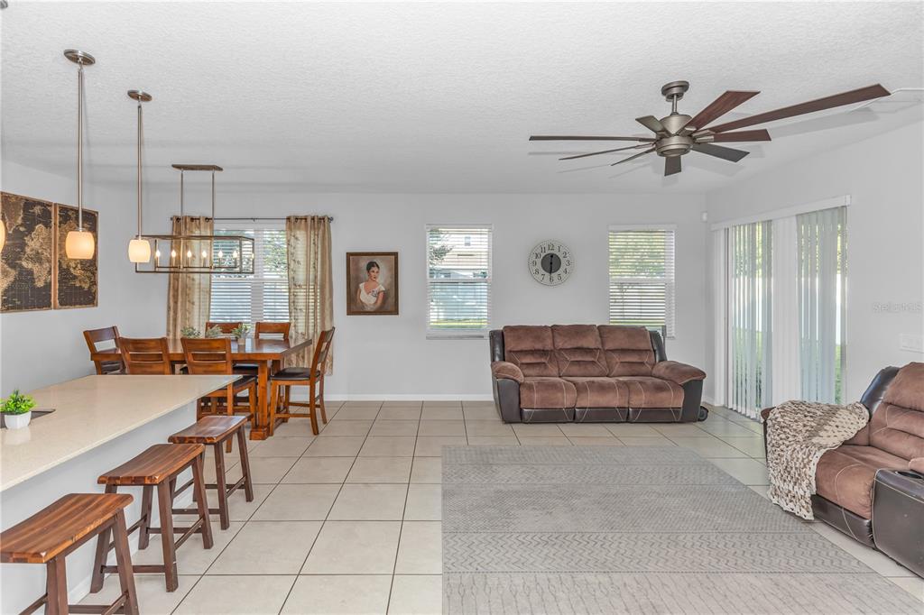 An open-concept living and dining area features tile floors, a kitchen island, and brown furniture — 3301 BETHPAGE LOOP, MOUNT DORA, FL