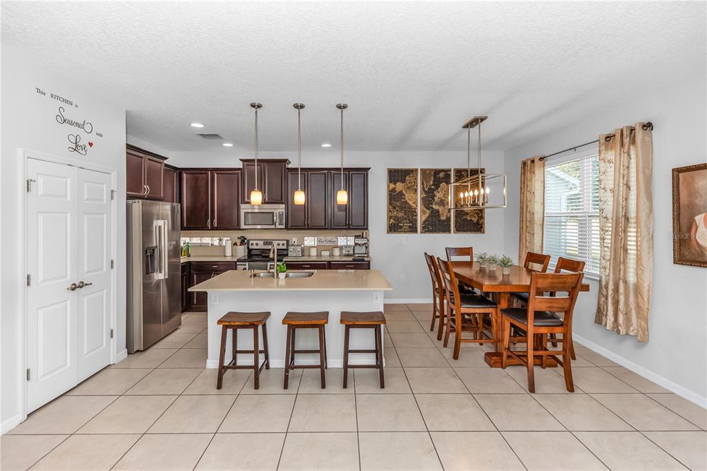 An open-concept kitchen and dining area features dark wood cabinets, a central island, and tile flooring — 3301 BETHPAGE LOOP, MOUNT DORA, FL