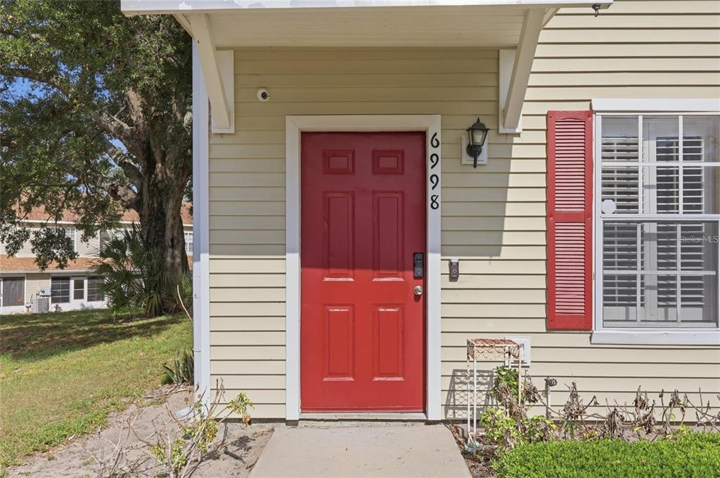 A red front door with the number 6998 is centered on the light-colored siding exterior — 6998 WOODLAKE DRIVE, ORLANDO, FL