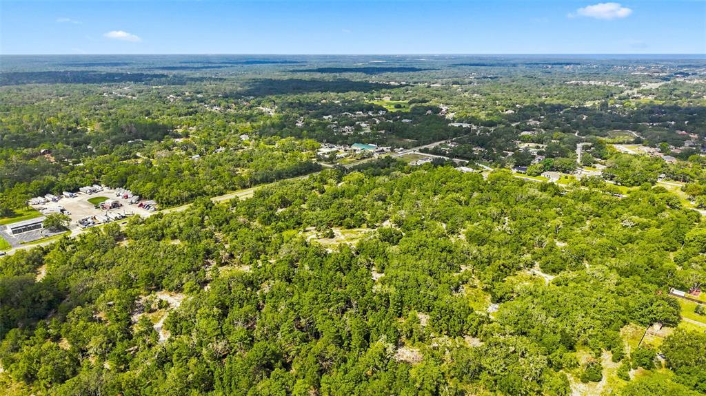 An aerial view shows a large, wooded lot next to a paved parking area — 8439 COUNTY LINE ROAD, SPRING HILL, FL