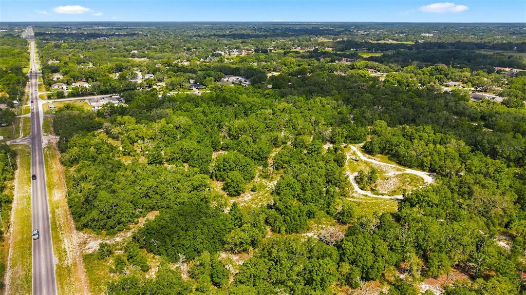 An aerial view shows a large, wooded plot of land adjacent to a paved road — 8439 COUNTY LINE ROAD, SPRING HILL, FL