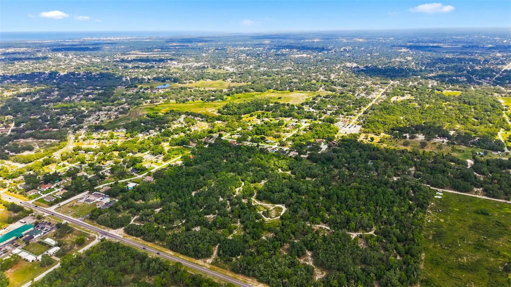 An aerial view shows a large, wooded plot of land adjacent to a suburban neighborhood — 8439 COUNTY LINE ROAD, SPRING HILL, FL