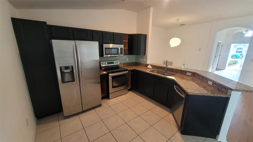 A kitchen with dark cabinets and a breakfast bar overlooks a living area with wood-look flooring — 7249 TWIN CEDAR LANE, LAKELAND, FL