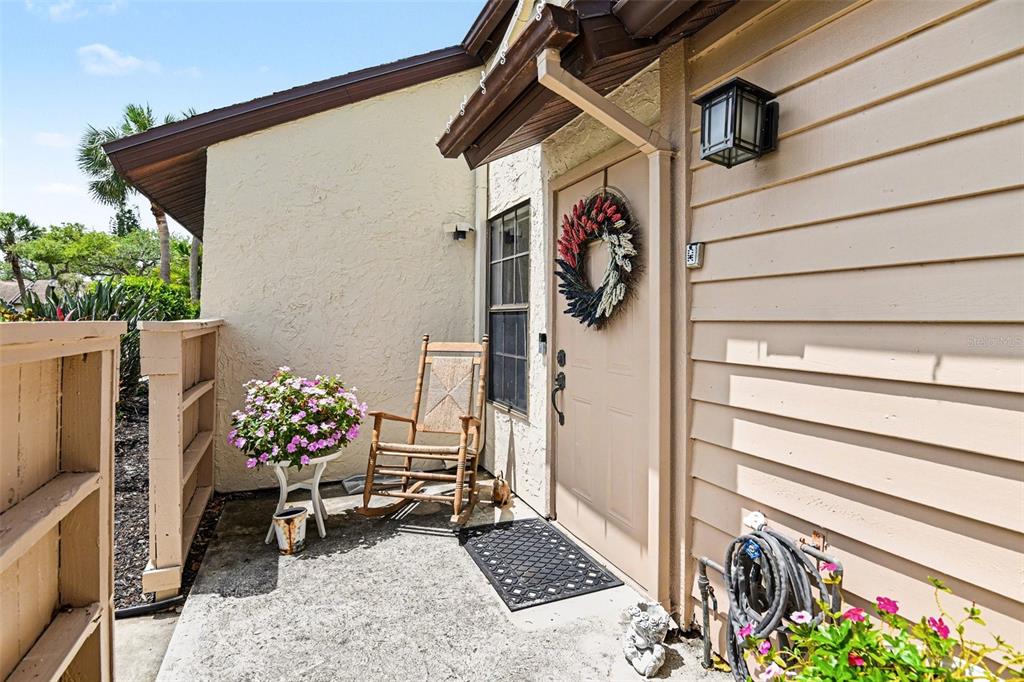 A tan front door with a wreath sits on a concrete porch with a rocking chair — 5401 BRASSY LOOP, NORTH PORT, FL