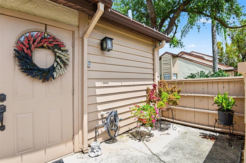 A beige exterior wall with a door, a wreath, potted plants, and a wooden fence — 5401 BRASSY LOOP, NORTH PORT, FL