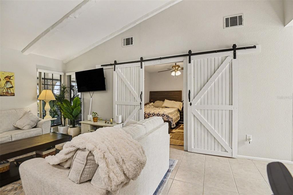 A living room with white barn doors opening into a bedroom with a bed — 5401 BRASSY LOOP, NORTH PORT, FL