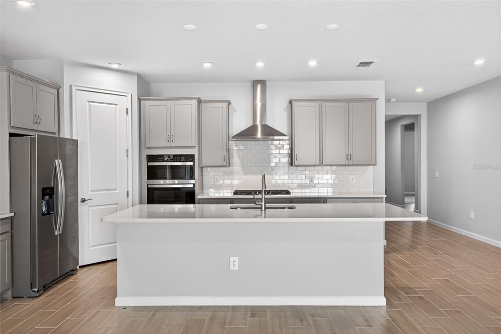 A modern kitchen features gray cabinets, a large island with a sink, and stainless steel appliances — 13136 OXEYE LANE, PARRISH, FL