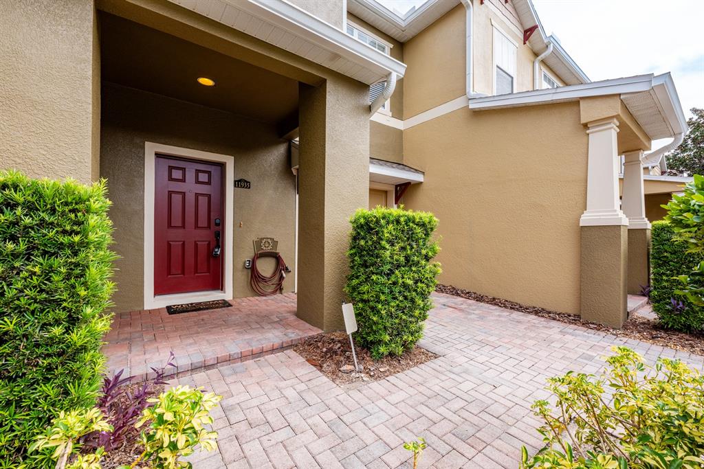 A red front door is set within a covered entryway featuring brick pavers and landscaping — 11935 GREAT COMMISSION WAY, ORLANDO, FL