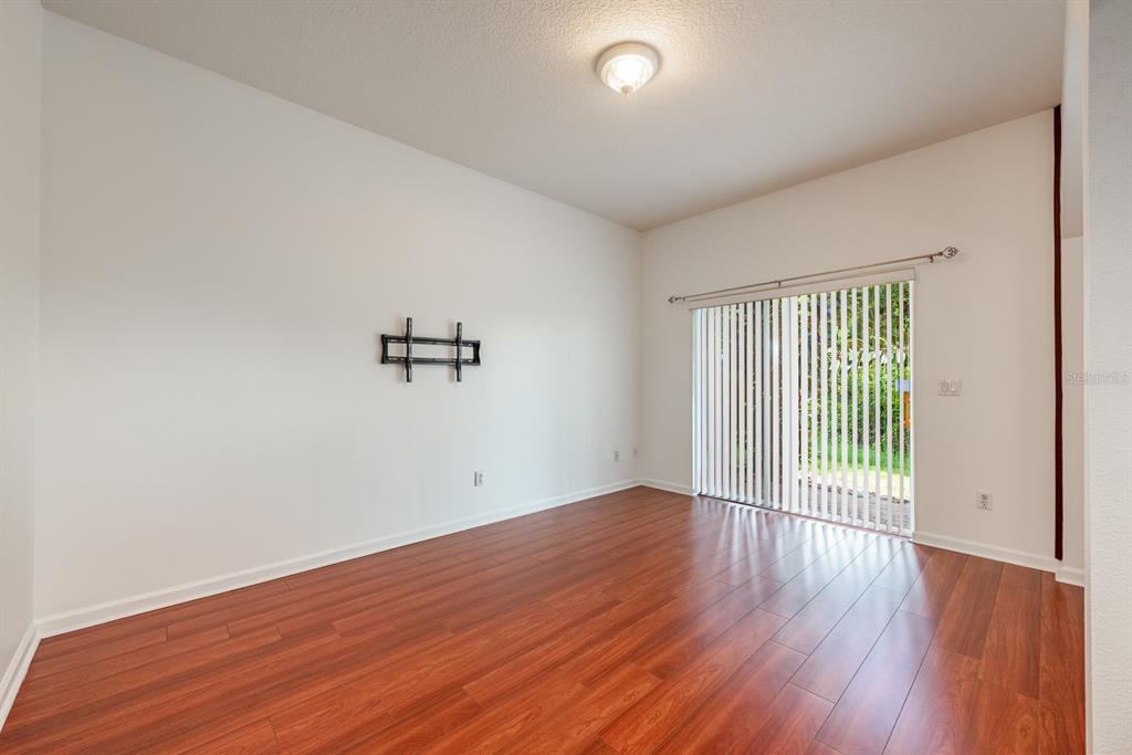 An empty room features wood-look flooring, white walls, a ceiling light, and sliding glass doors — 11935 GREAT COMMISSION WAY, ORLANDO, FL