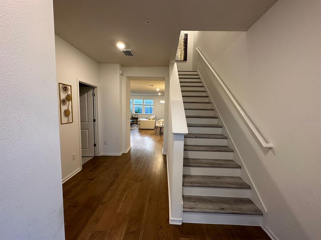 A foyer features hardwood floors, a staircase with gray treads, and a view into a living area — 14475 SAPELO BEACH DRIVE, ORLANDO, FL