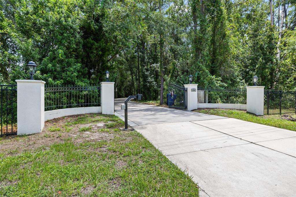 A concrete driveway leads through an open wrought iron gate flanked by four white pillars — 6800 WISTERIA LOOP, LAND O LAKES, FL