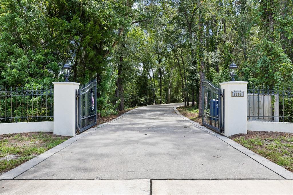A concrete driveway leads through an open metal gate flanked by two white pillars — 6800 WISTERIA LOOP, LAND O LAKES, FL