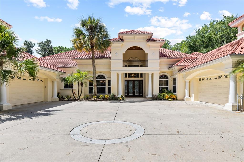A large, beige Mediterranean-style house with a red tile roof and a spacious concrete driveway — 6800 WISTERIA LOOP, LAND O LAKES, FL