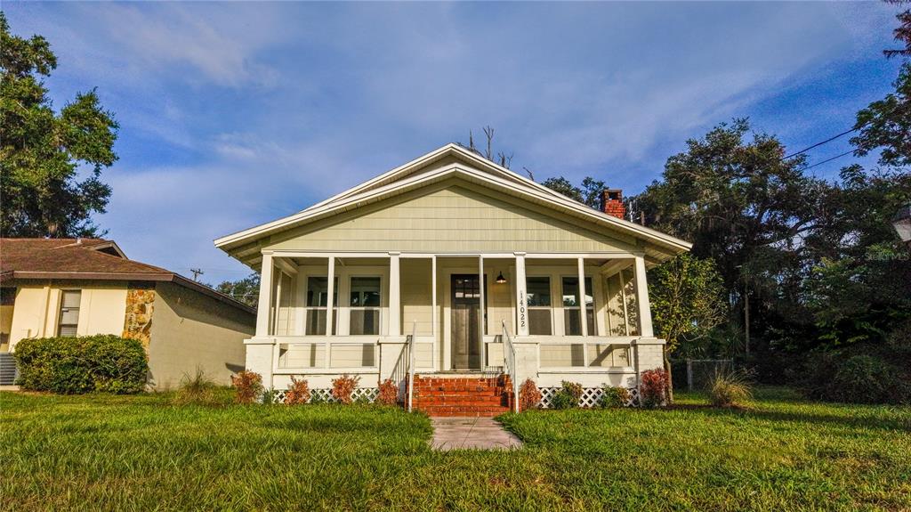 A light green bungalow with a front porch and brick steps sits on a grassy lawn — 14022 4TH STREET, DADE CITY, FL
