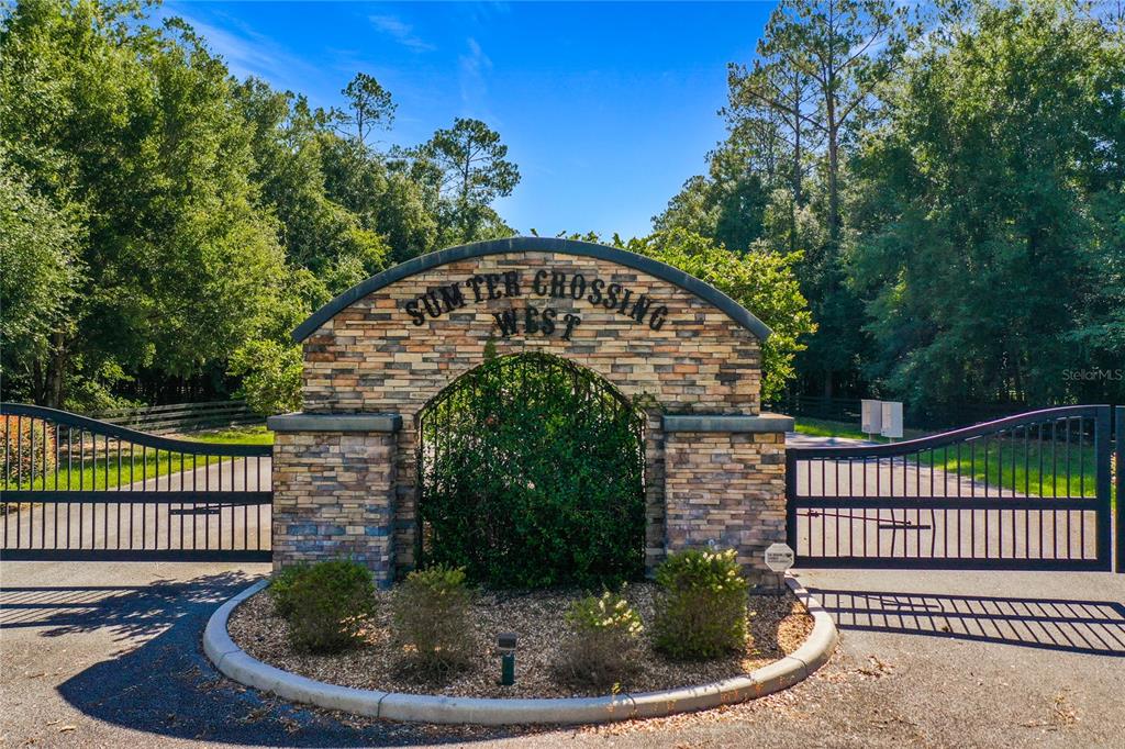 A stone entrance monument with a gated driveway stands before a wooded area — 10620 NE 104TH CIRCLE, OXFORD, FL