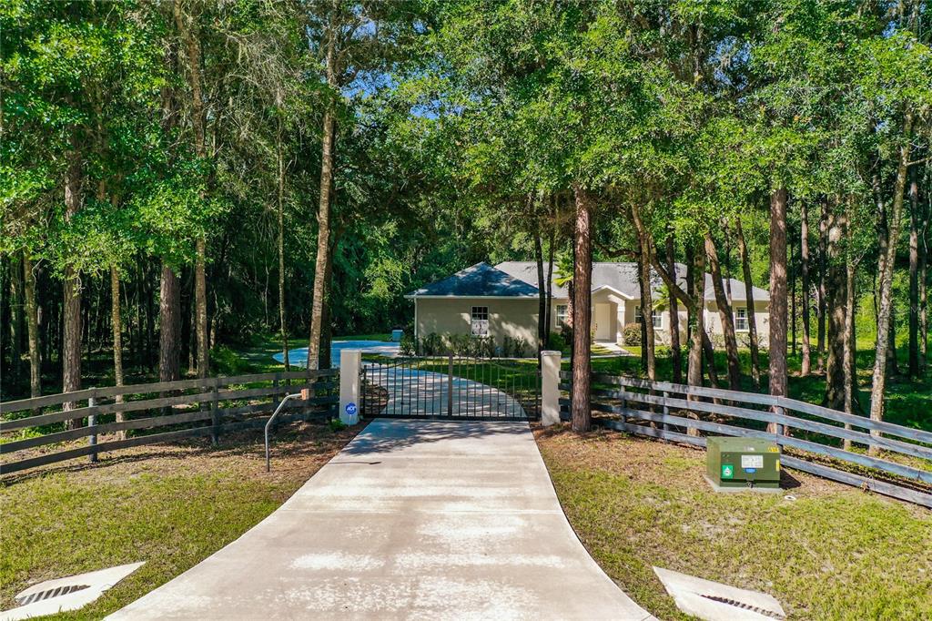 A gated concrete driveway leads to a single-story house surrounded by trees and a fence — 10620 NE 104TH CIRCLE, OXFORD, FL
