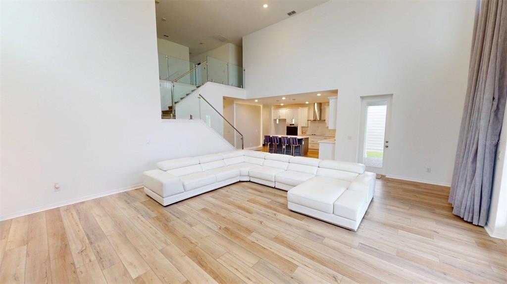 A spacious living room features a large white sectional sofa, light wood flooring, and stairs — 17242 LAKE STAR ROAD, WINTER GARDEN, FL