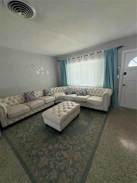 A living room features a large tufted sectional sofa, matching ottoman, and teal curtains — 52 45TH AVENUE, ST PETE BEACH, FL