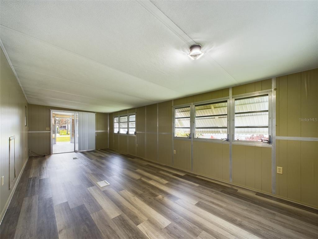 A sunroom with wood-look flooring, paneled walls, jalousie windows, and a sliding glass door — 3502 DELAWARE AVENUE, SEBRING, FL