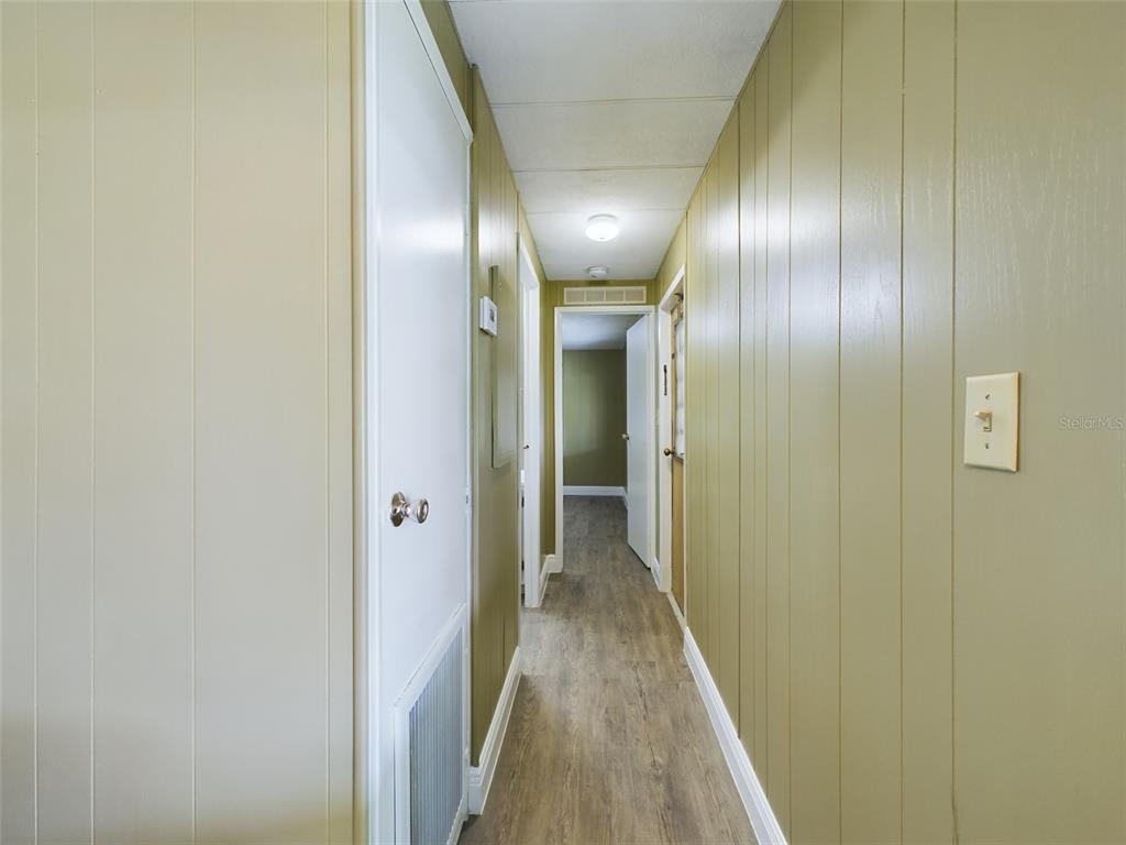 A narrow hallway features light green wood-paneled walls, white trim, and wood-look flooring — 3502 DELAWARE AVENUE, SEBRING, FL