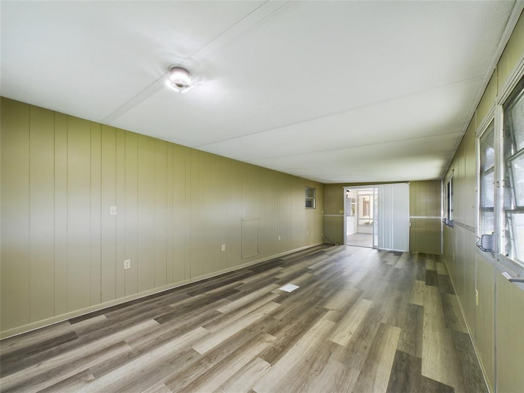 An empty room with olive green paneled walls, wood-look flooring, and a sliding glass door — 3502 DELAWARE AVENUE, SEBRING, FL
