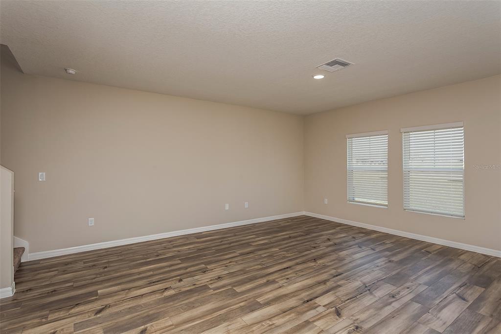 An empty room features wood-look flooring, beige walls, and two windows with white blinds — 15257 MAUDE LANDING LOOP, WIMAUMA, FL